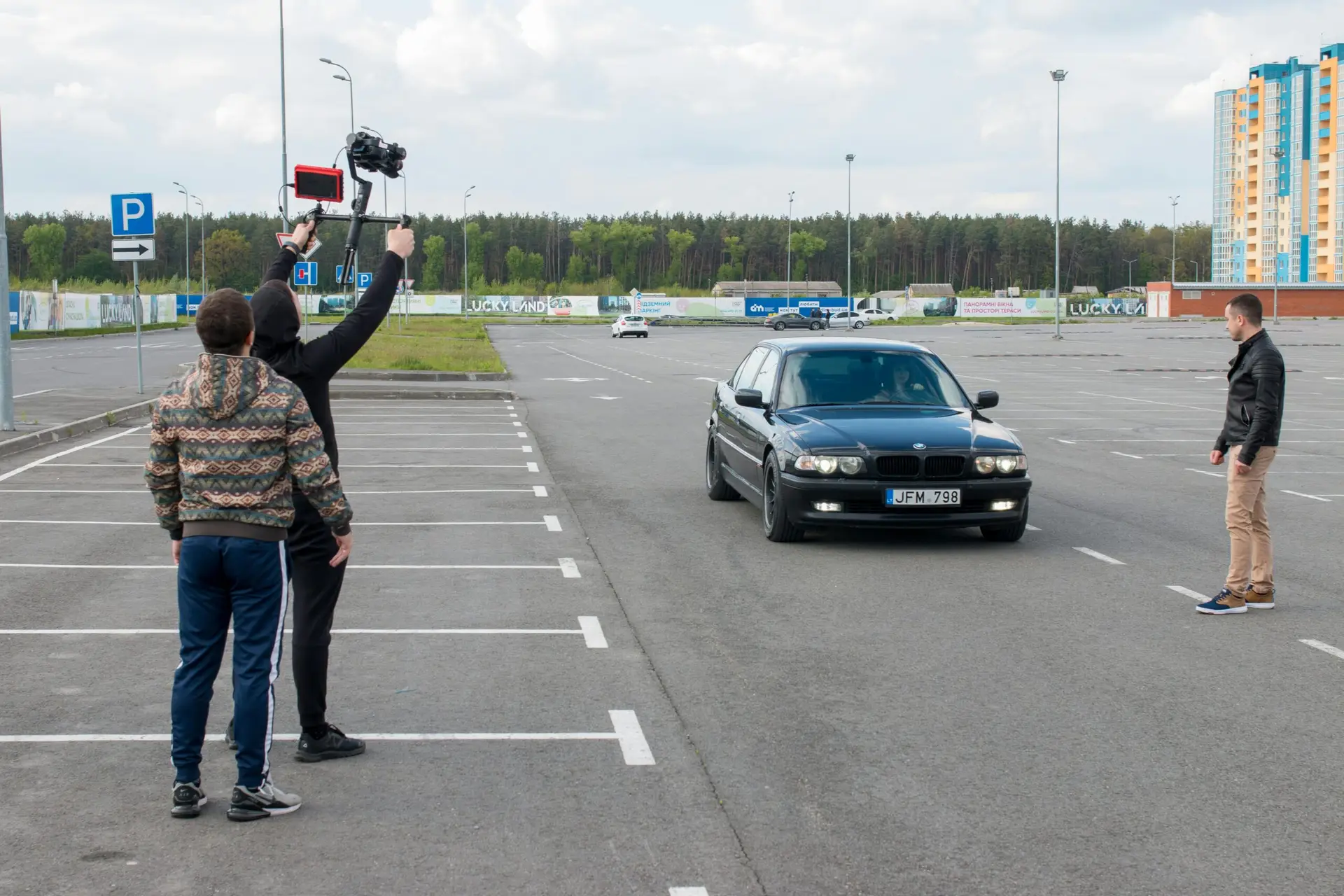 A film crew with a camera rig directs a car scene in an outdoor parking lot.